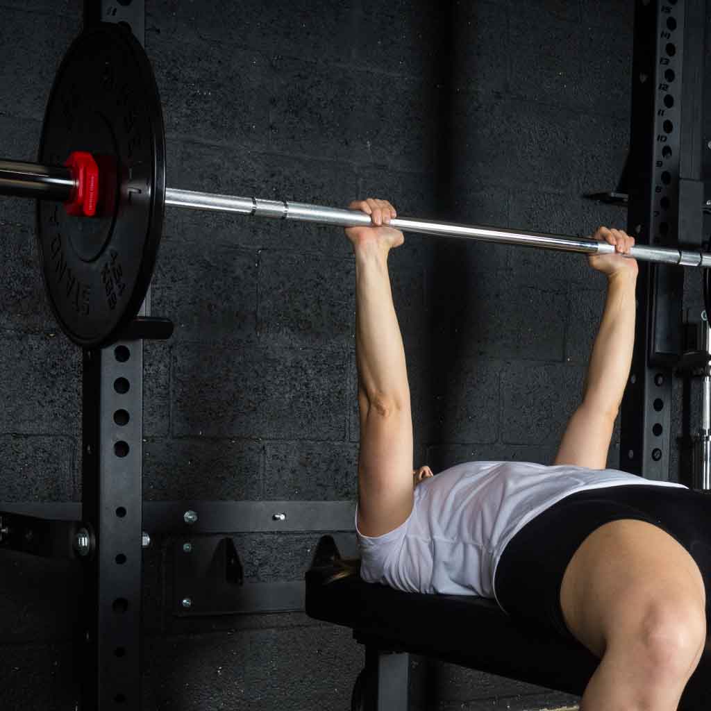 Barbell Standard 1000 barbell bench press with black plates and red magnetic collars in home gym setup