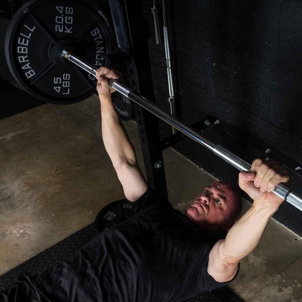 Man bench pressing with Barbell Standard 1500 Olympic bar in gym setup.