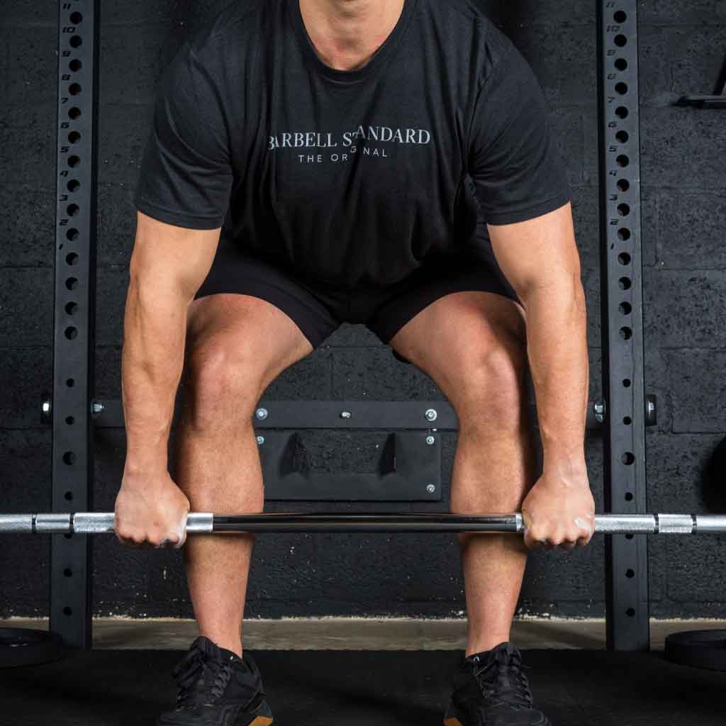 Man in Barbell Standard shirt setting up for deadlift with Olympic barbell in gym.