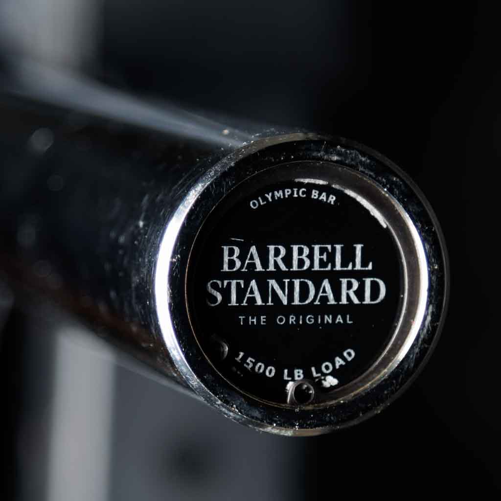 Barbell Standard Olympic bar close-up of endcap with logo and text reading 1500 lb load against a dark background