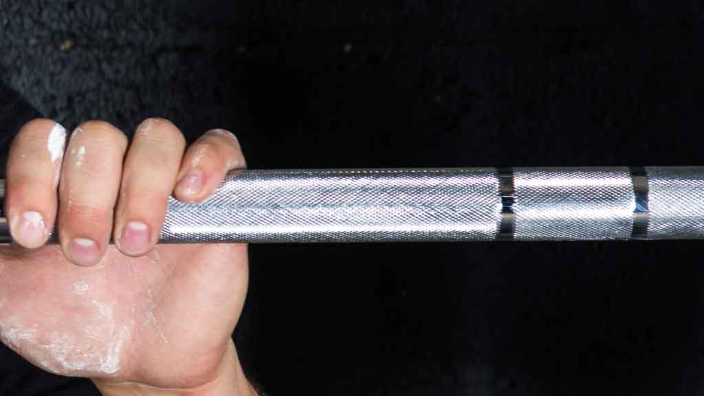 Barbell Standard 1500 barbell knurling close up with athlete grip and chalk for secure lift control