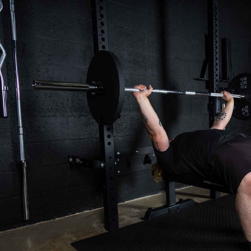 Athlete performing bench press with Barbell Standard Olympic barbell racked in power cage inside gym