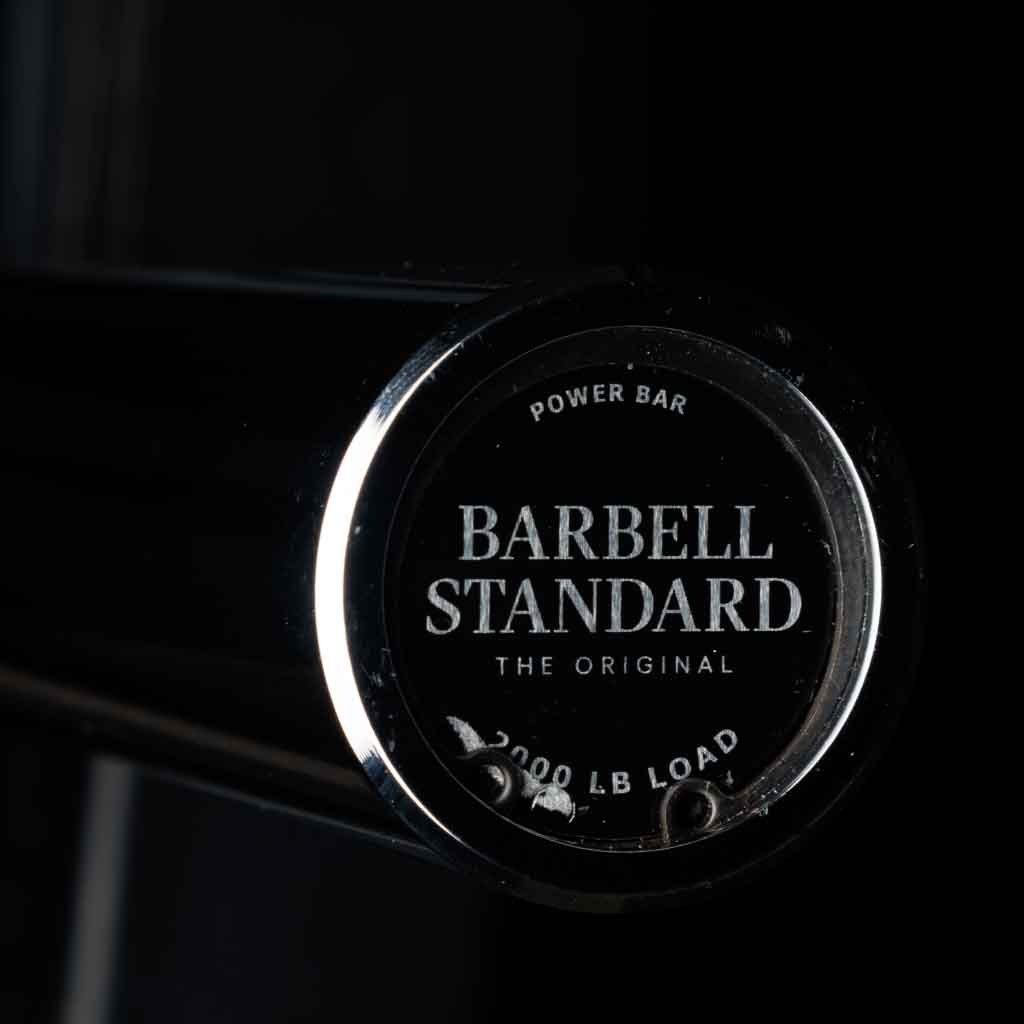 Barbell Standard Olympic power bar close-up of endcap with logo and text reading 2000 lb load against a dark background
