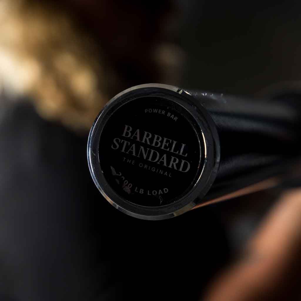 Close up of Barbell Standard Power Bar endcap showing logo and 200 lb load rating with blurred background