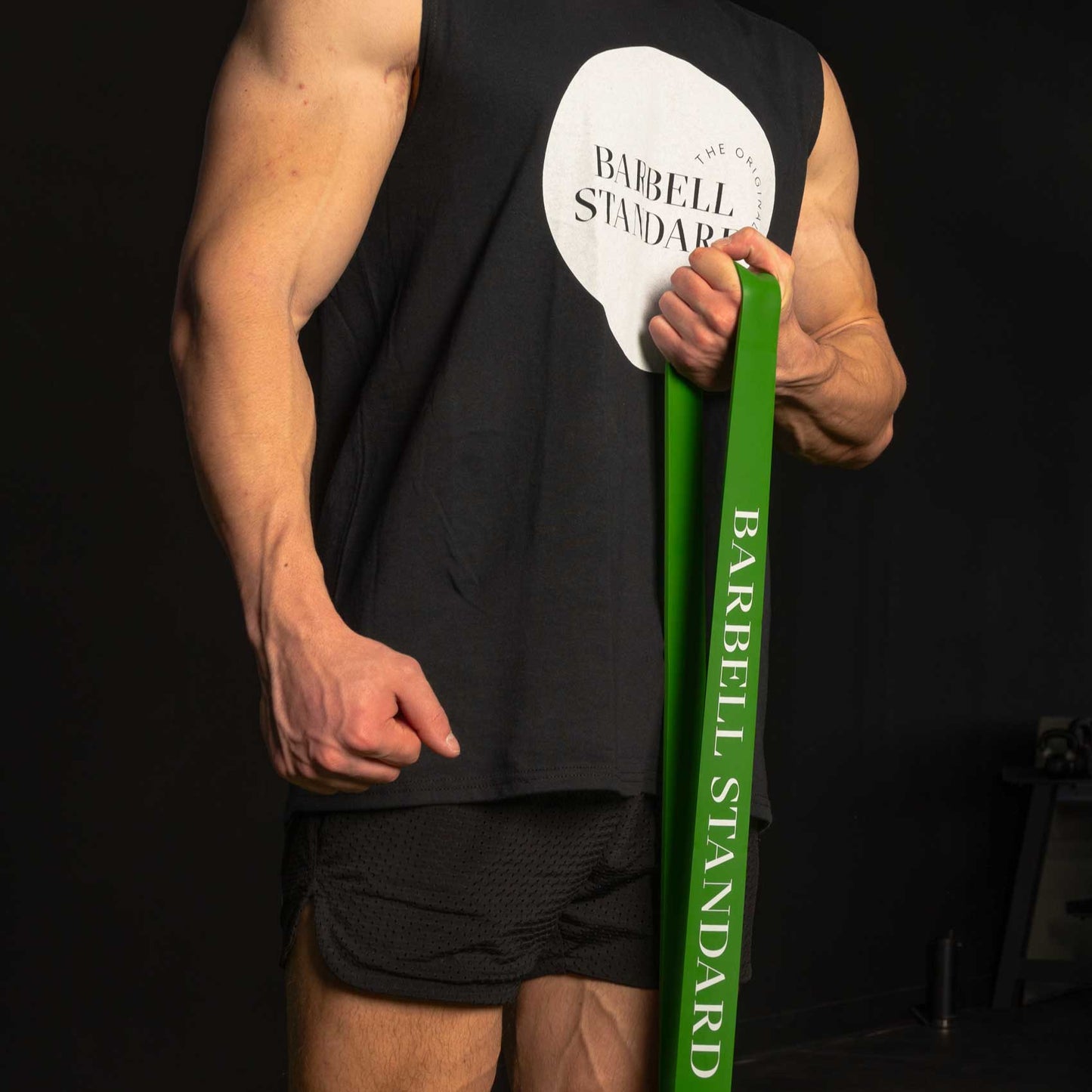 Athlete using green Barbell Standard resistance band while wearing branded workout tank