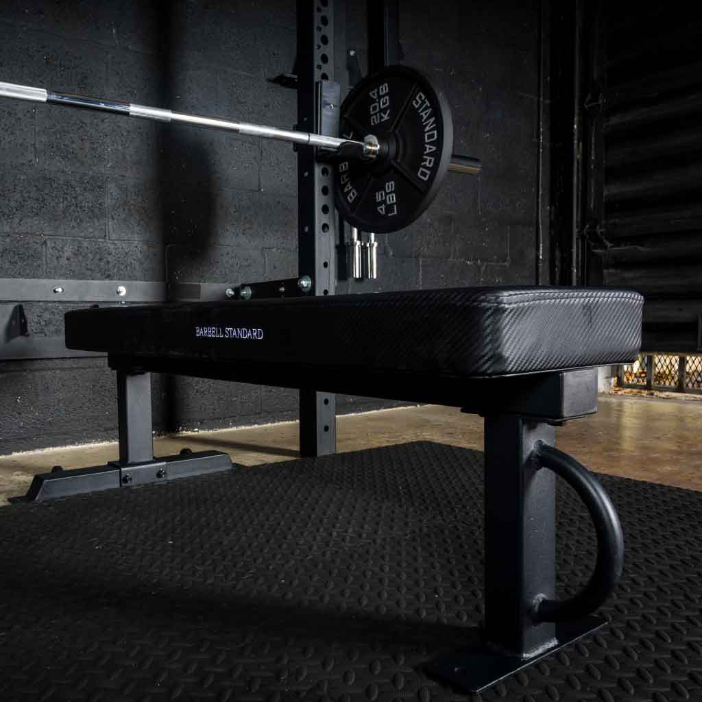 Barbell Standard competition flat weight bench with carbon fiber style pad and loaded barbell on squat rack in gym setting
