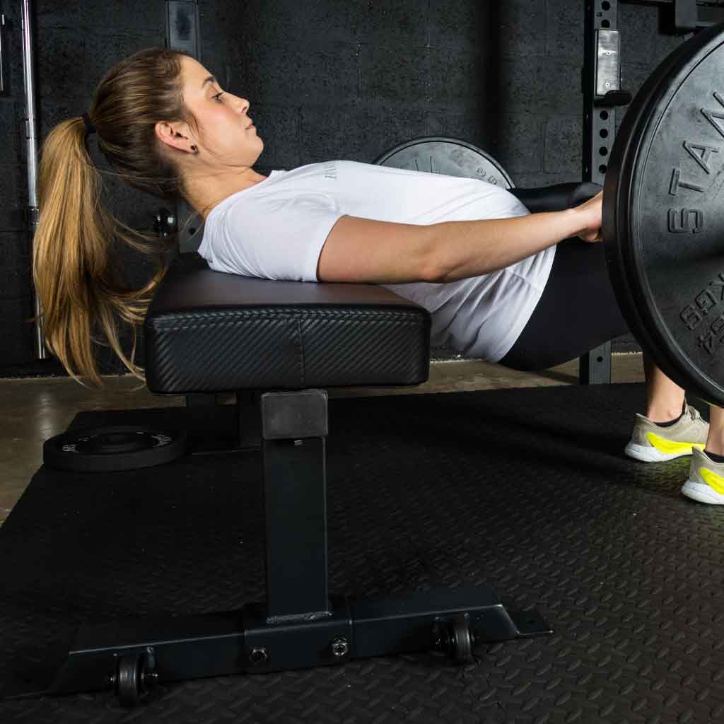 Woman performing hip thrust on Barbell Standard competition flat bench with loaded barbell across hips