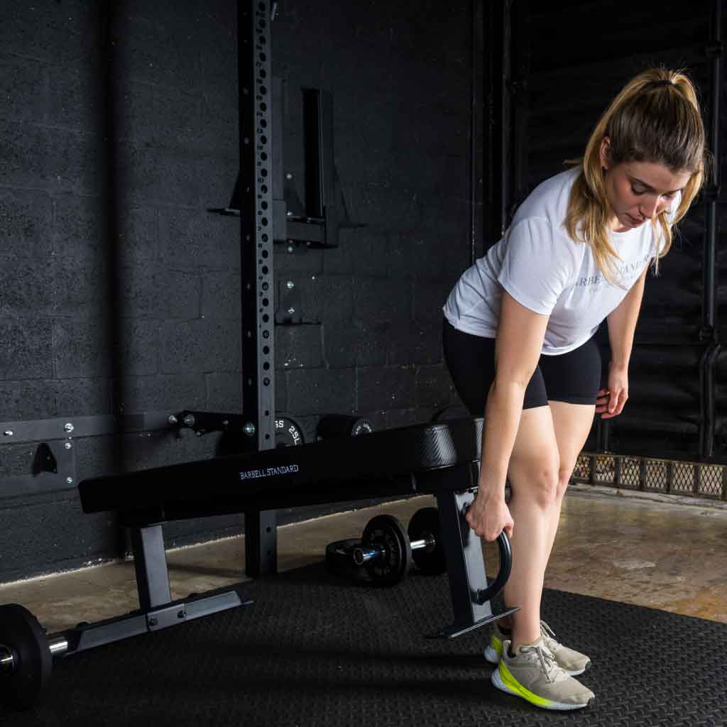 Woman lifting and moving Barbell Standard competition flat weight bench using built-in handle and wheels
