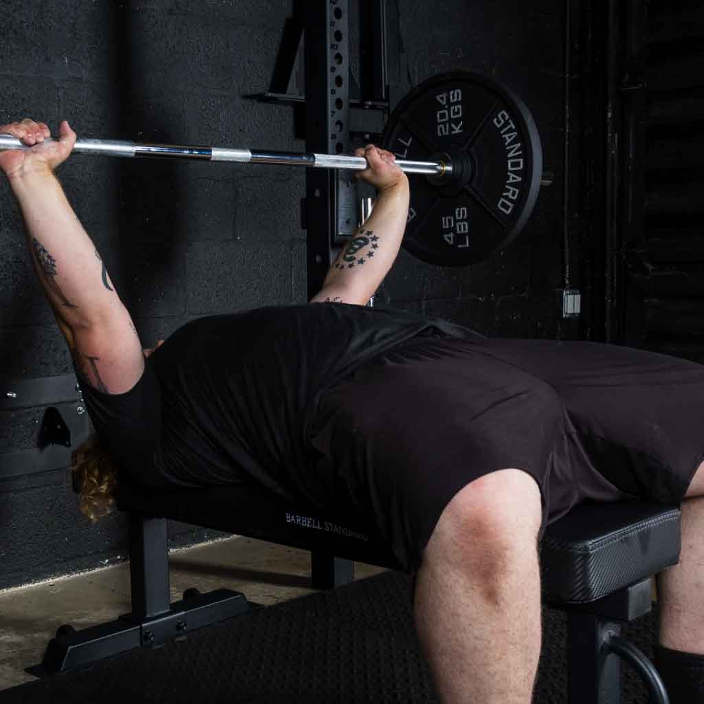 Man performing bench press on Barbell Standard competition flat bench with 45 lb iron weight plates on barbell