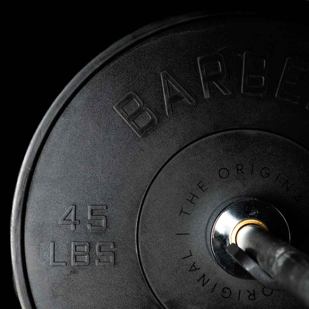 A set of black Olympic bumper plates with raised lettering and the Barbell Standard logo on the center.