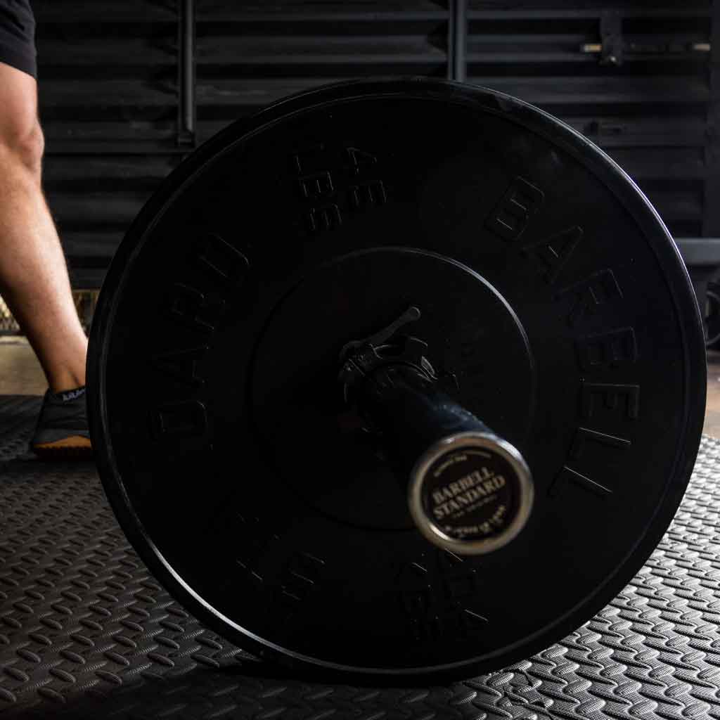Barbell Standard 45 lb rubber bumper plate loaded on barbell resting on gym floor with athlete preparing to lift