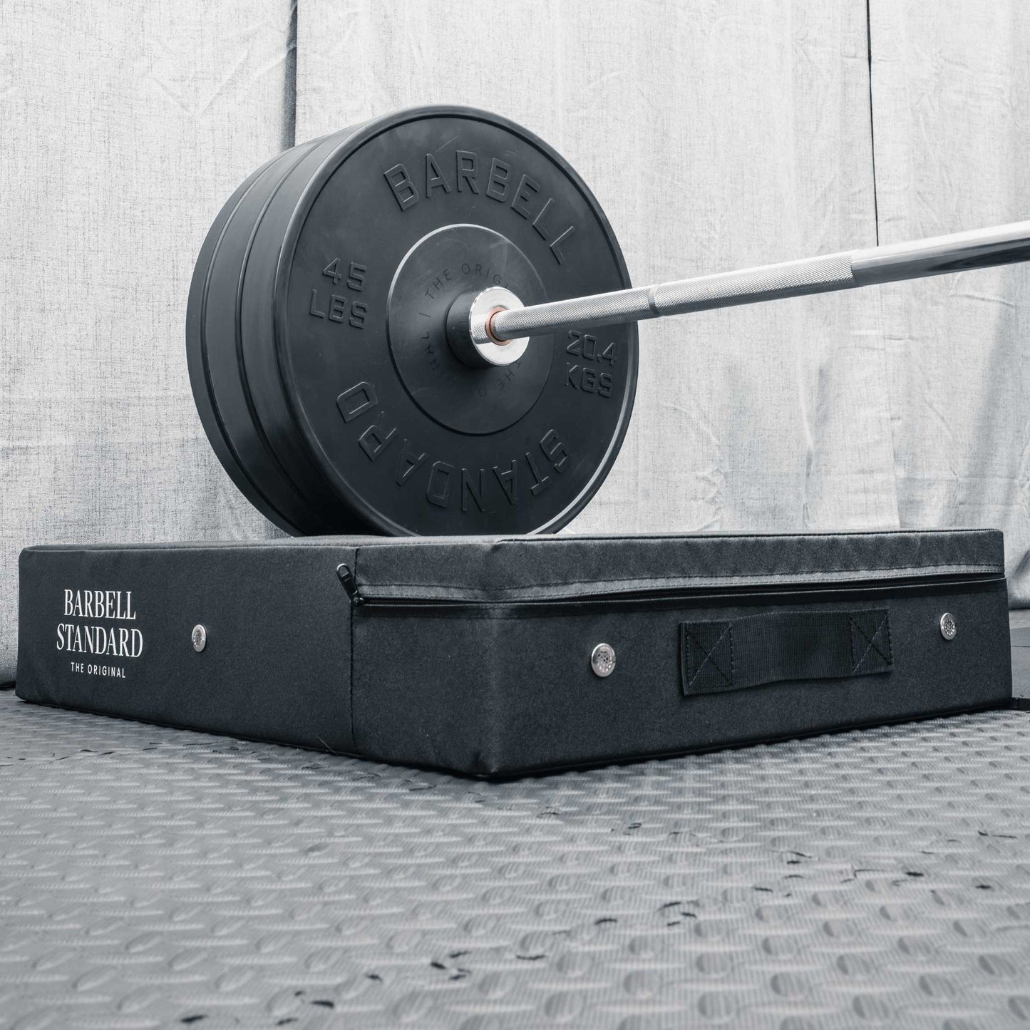 Olympic barbell loaded with Barbell Standard 45 lb weight plates resting on black drop pad