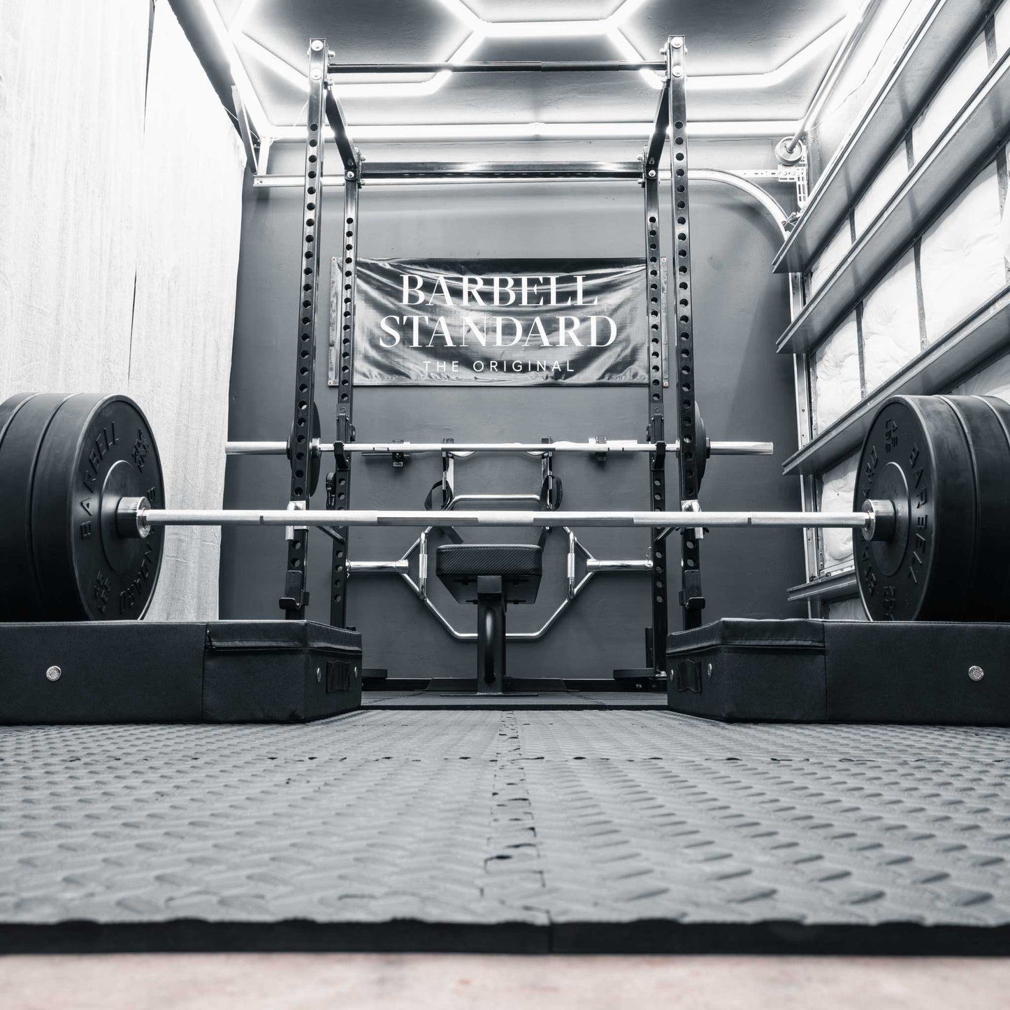Barbell Standard Olympic barbell loaded with weight plates resting on drop pads inside a home gym power rack