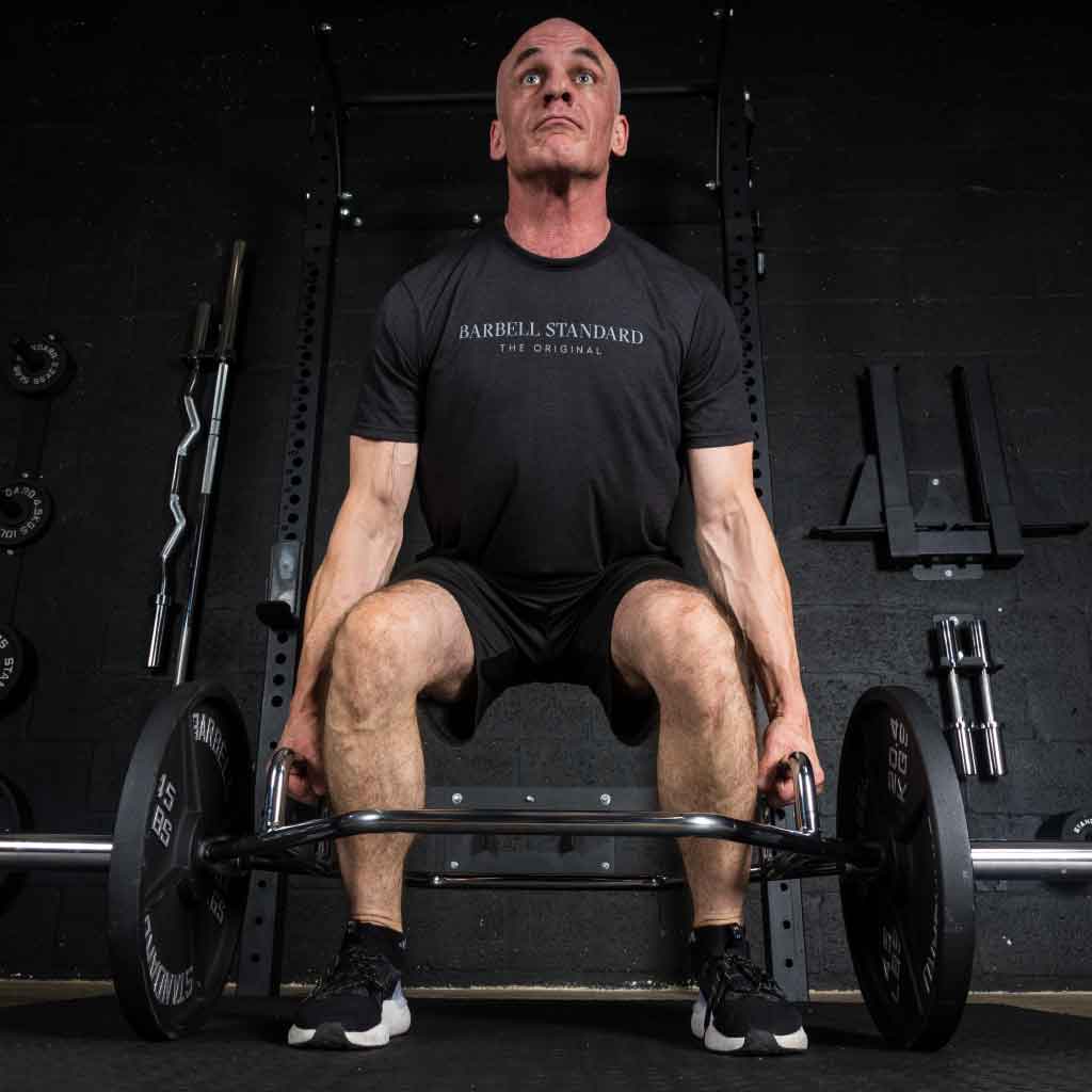 Man performing deadlift with Barbell Standard hex trap bar and iron weight plates in a home gym