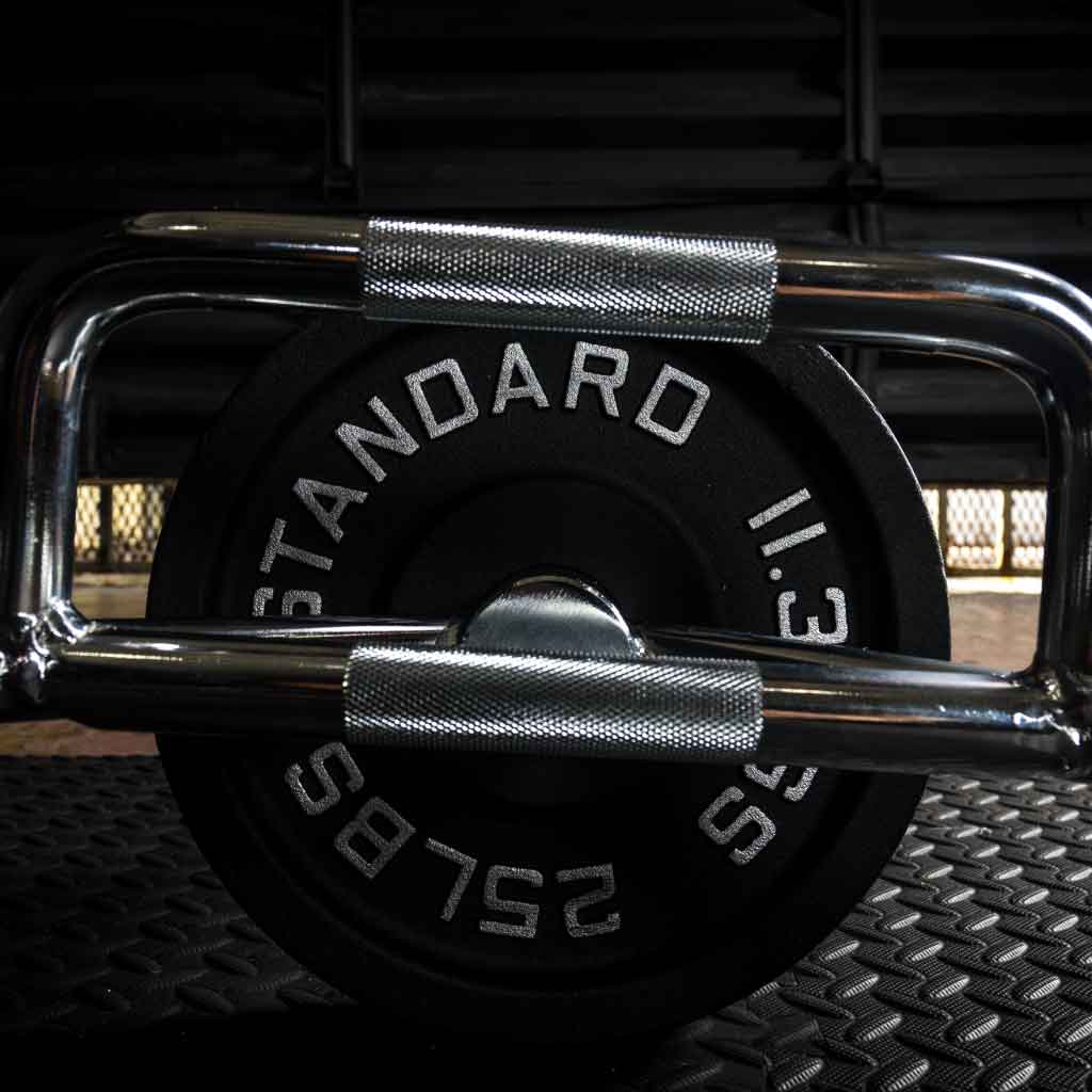 Barbell Standard hex trap bar with knurled handles loaded with 25 lb plates resting on gym flooring