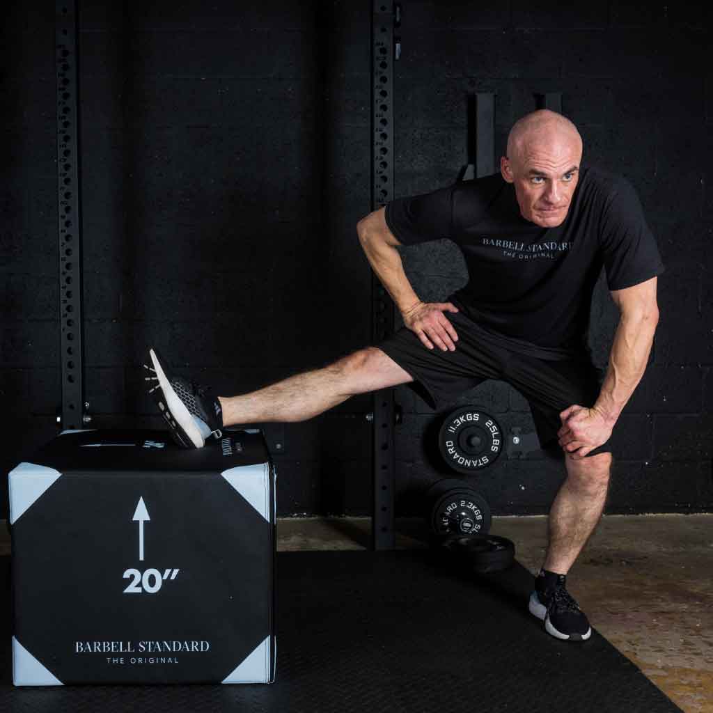 Man stretching hamstrings with foot elevated on Barbell Standard 20-inch foam plyo jump box in gym setting