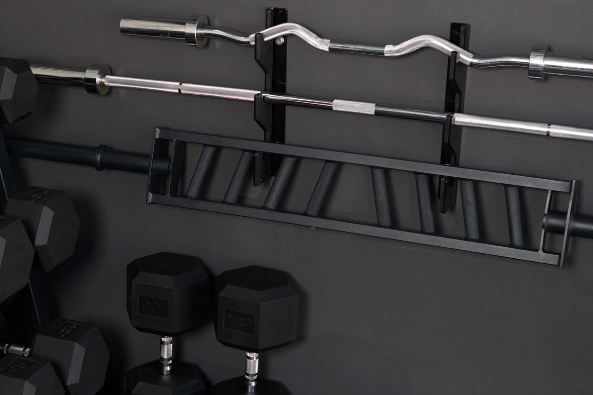 Barbells and specialty bars on a wall rack above rubber hex dumbbells