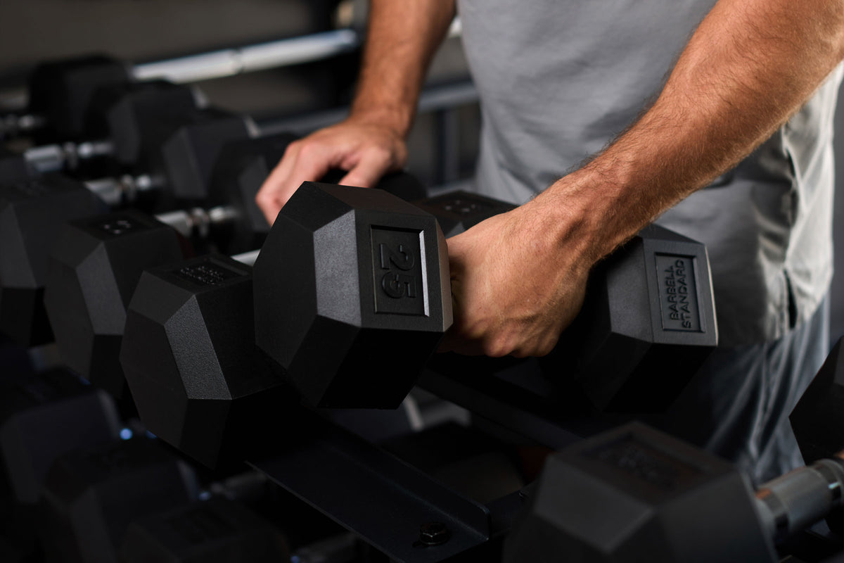 Lifter taking a pair of 25 lb rubber hex dumbbells off a dumbbell rack