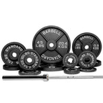 A variety of black free weights and a barbell with weight plates arranged in front of a white background.